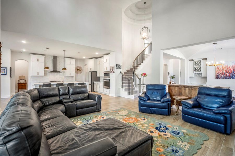 This spacious living area features high ceilings, a modern open floor plan, and abundant natural light. It includes a sleek kitchen and a striking spiral staircase as a focal point.