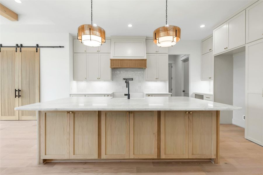 Dual tone kitchen with a large island with sink, a barn door, light wood-style floors, light stone counters, and dual tone cabinetry