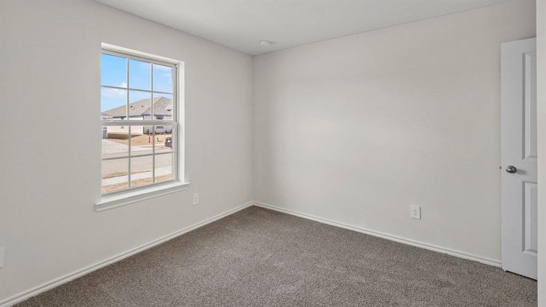 Bright room featuring a grid-pattern window, neutral wall paint, gray carpet flooring, white baseboards, and a white interior door