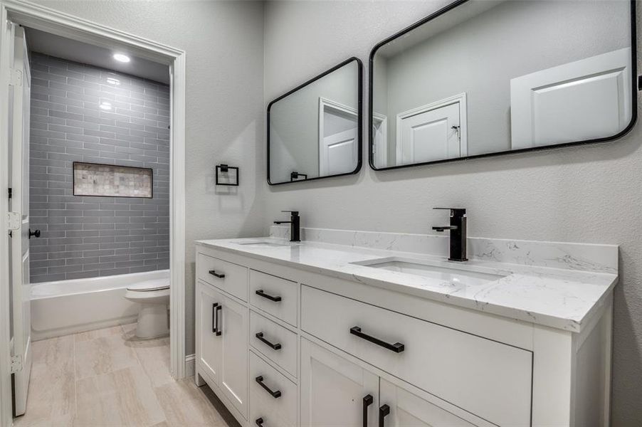 Bathroom featuring double vanity, a textured wall, and shower combination Bathroom featuring double vanity, a textured wall, and shower combination