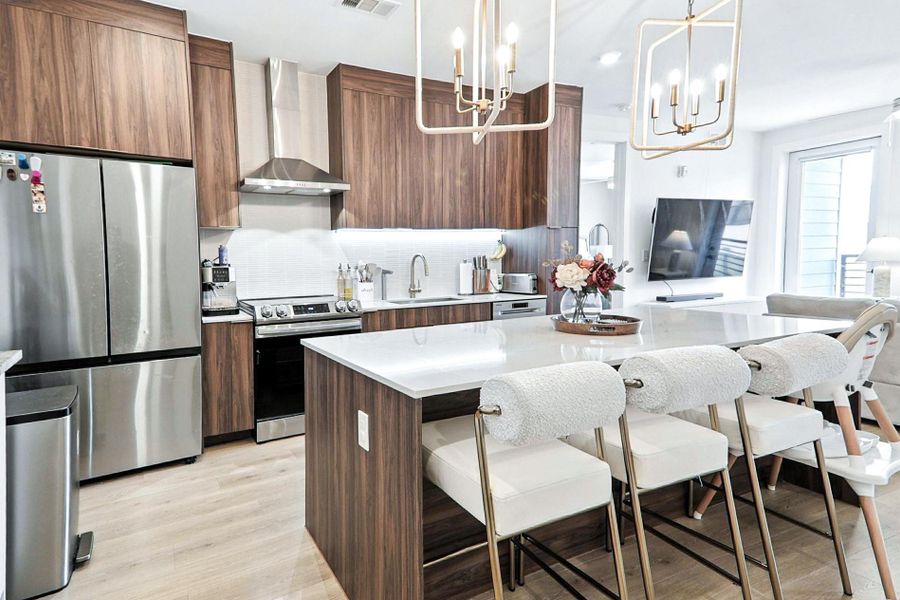 Kitchen featuring stainless steel appliances, decorative backsplash, wall chimney exhaust hood, a kitchen island, and a breakfast bar