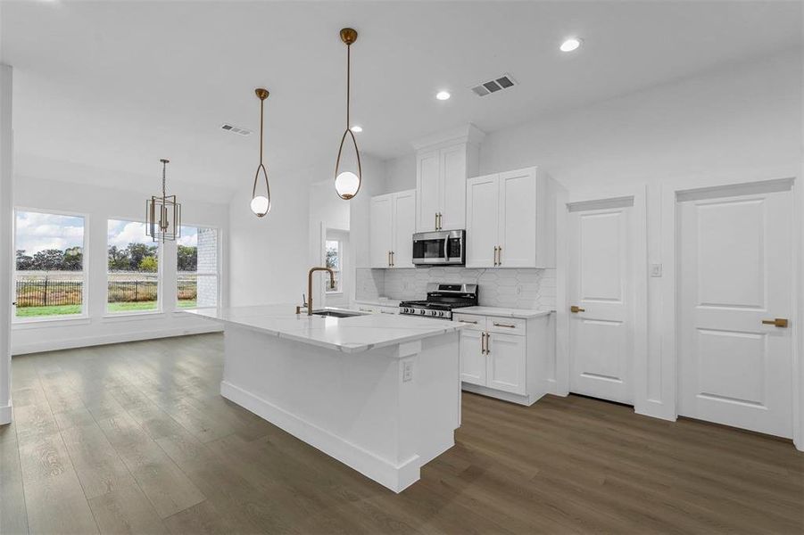 Kitchen with dark wood-type flooring, appliances with stainless steel finishes, white cabinetry, backsplash, and recessed lighting Kitchen with dark wood-type flooring, appliances with stainless steel finishes, white cabinetry, backsplash, and recessed lighting