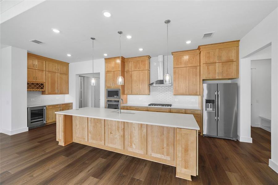 Expansive kitchen featuring wood-finish flooring, light wood cabinetry, and a large central island with a light-toned countertop