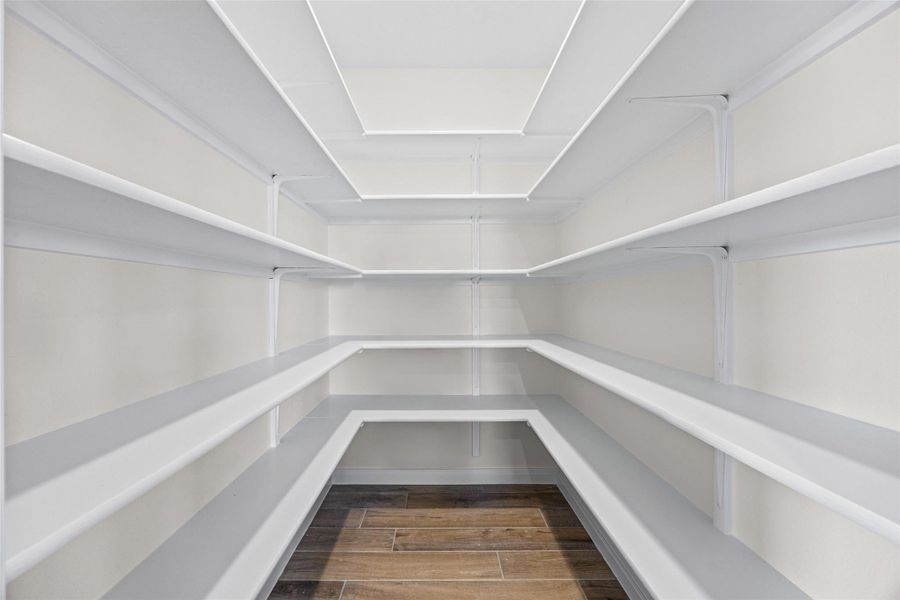 Ample built-in shelving wraps around this walk-in storage area featuring wood-look tile flooring. Ample built-in shelving wraps around this walk-in storage area featuring wood-look tile flooring.