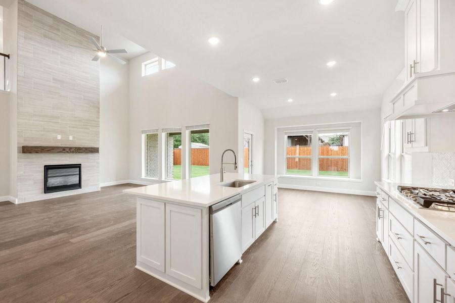 Open-concept kitchen with white island, hardwood floors, and tile fireplace in adjoining living area with vaulted ceiling