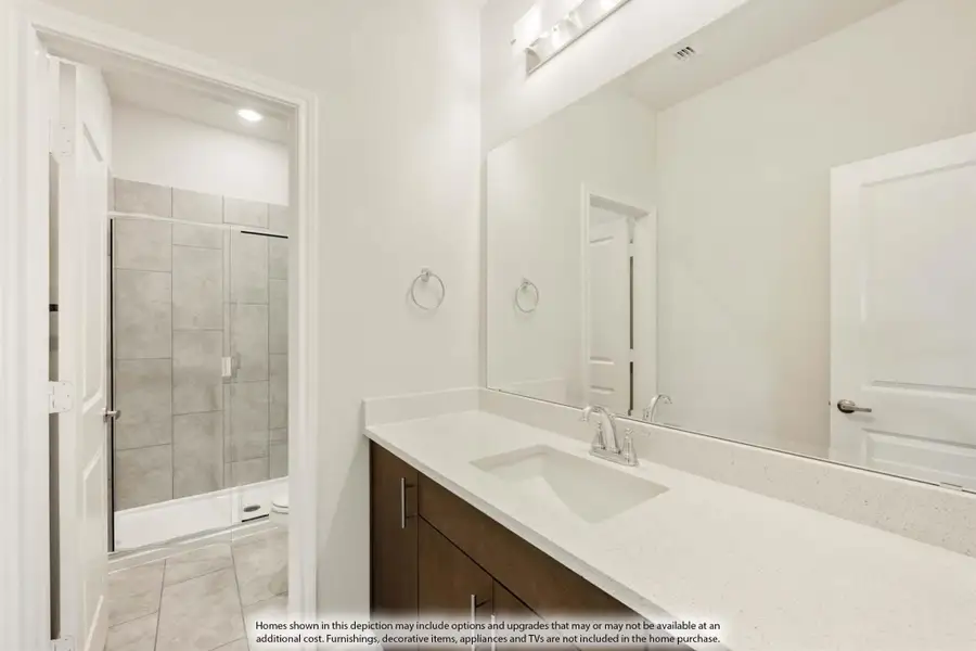 Bathroom with quartz countertop, dark wood vanity, large mirror, and tiled walk-in shower visible through doorway Bathroom with quartz countertop, dark wood vanity, large mirror, and tiled walk-in shower visible through doorway