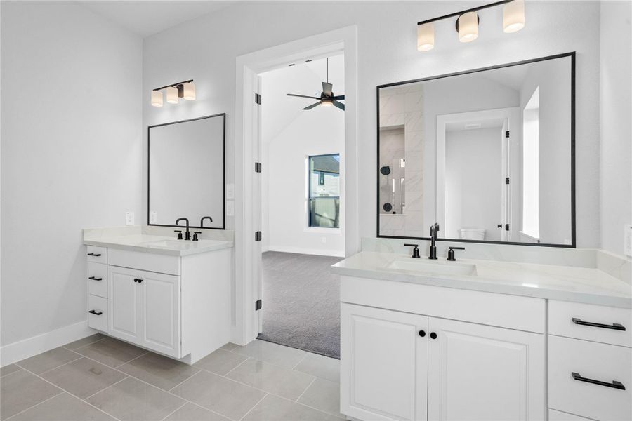 Modern primary bath features dual vanities with sleek bright white cabinetry, a quartz countertop, and matte black fixtures and hardware for a truly contemporary feel.