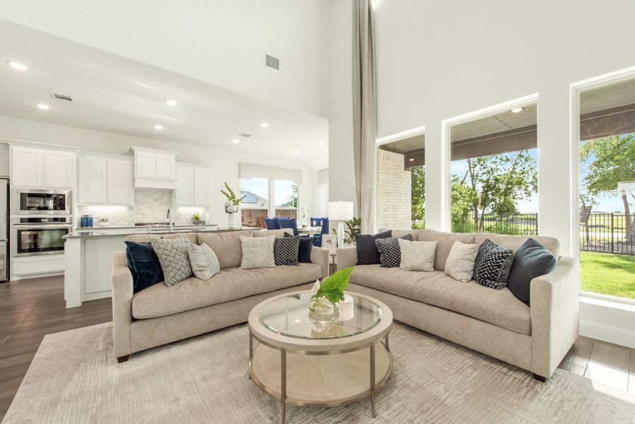 Open-concept living room with sectional sofa, high ceilings, and kitchen visible in background