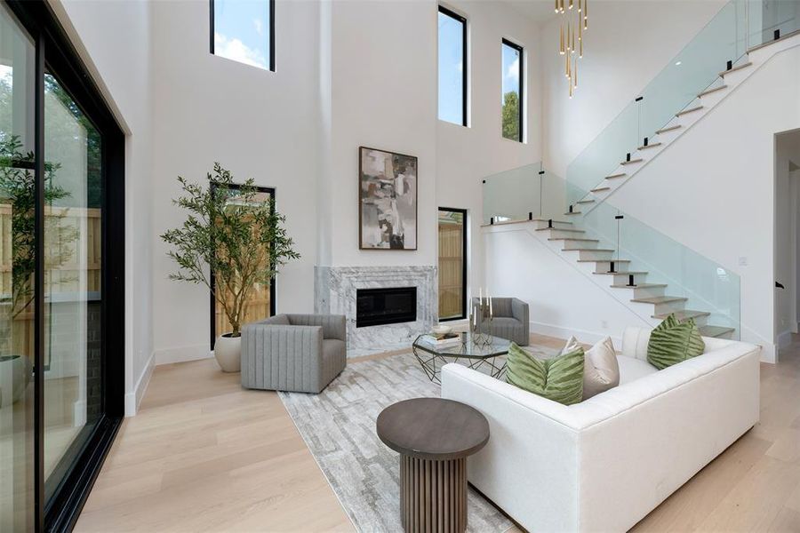 Living room with a high end fireplace, light wood-type flooring, a high ceiling, and stairway Living room with a high end fireplace, light wood-type flooring, a high ceiling, and stairway