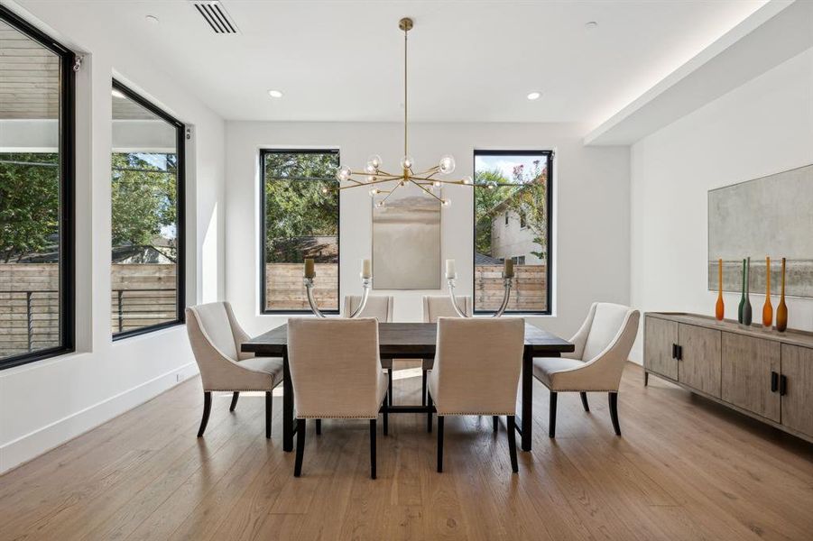 In the dining room, large picture windows with dark frames fill the room with natural light, offering views of the outdoors. A striking brass Arhaus branded chandelier with multiple glass spheres hangs from the ceiling, serving as the focal point of the space. The integrated LED lighting along the ceiling adds dimension.