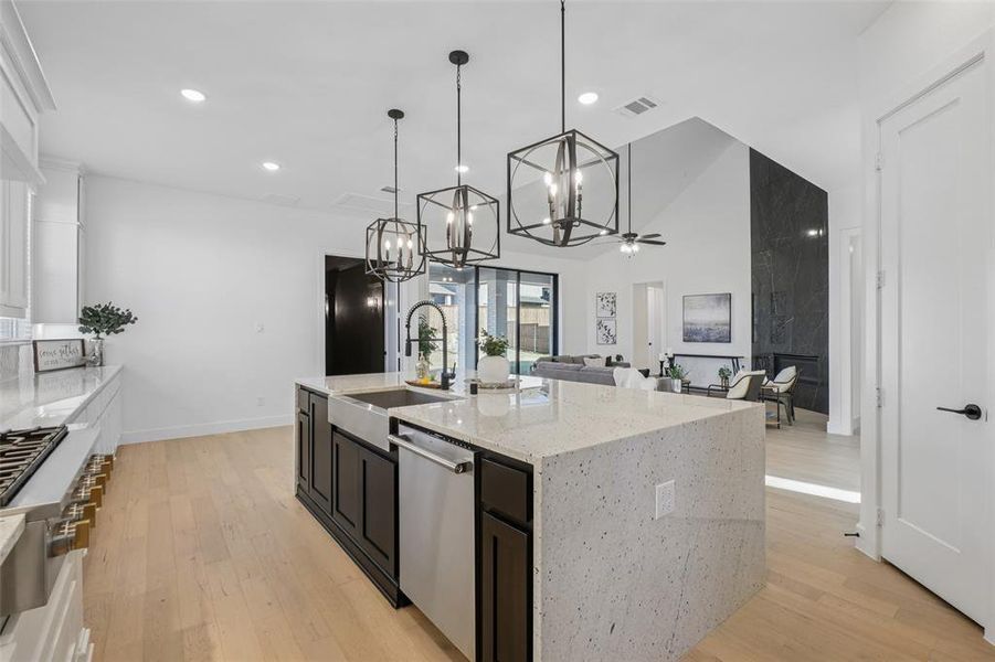 Kitchen featuring light stone counters, light wood-style floors, appliances with stainless steel finishes, dark cabinets, and pendant lighting Kitchen featuring light stone counters, light wood-style floors, appliances with stainless steel finishes, dark cabinets, and pendant lighting