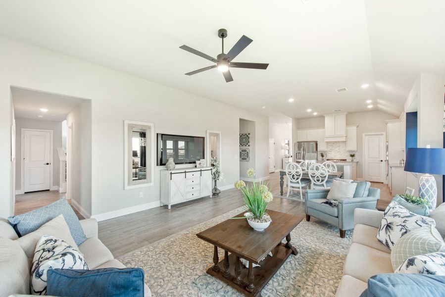 Open-concept living room with hardwood floors, ceiling fan, and kitchen visible in background