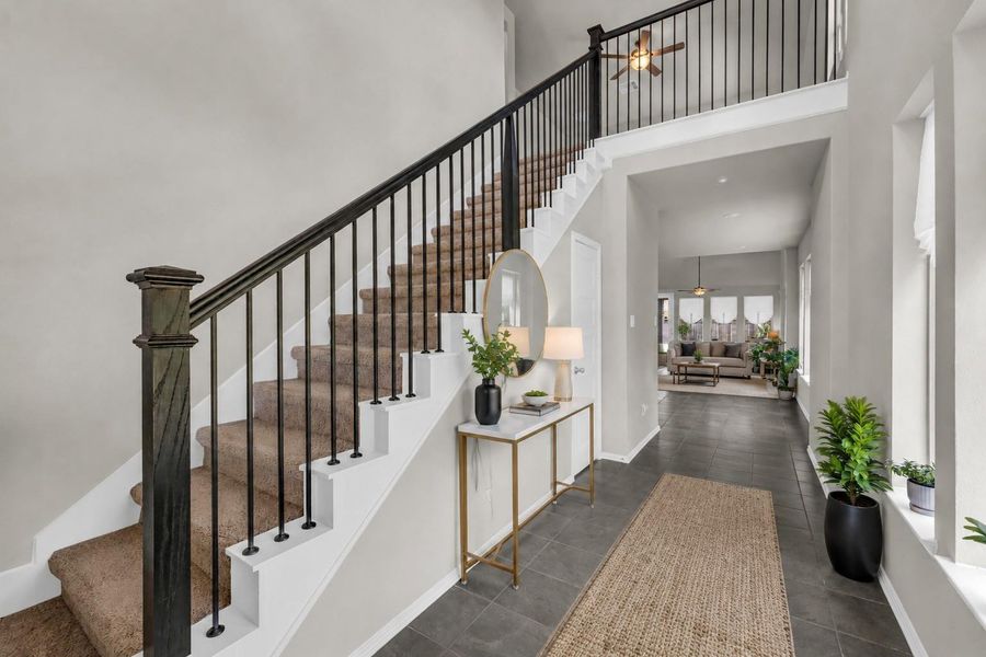 An inviting entryway with dark tile flooring leads from the entry to the living areas, featuring a carpeted staircase on one side and large windows providing natural light on the other.**Virtually staged An inviting entryway with dark tile flooring leads from the entry to the living areas, featuring a carpeted staircase on one side and large windows providing natural light on the other.**Virtually staged