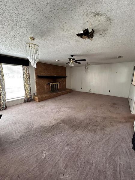 Unfurnished living room featuring carpet, a brick fireplace, a chandelier, a textured ceiling, and ceiling fan Unfurnished living room featuring carpet, a brick fireplace, a chandelier, a textured ceiling, and ceiling fan
