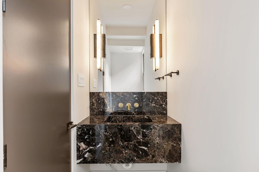Stepping into the powder tucked off the entry, a marble Fior di Bosco vanity, marble sconces, and espresso door anchor the space. Stepping into the powder tucked off the entry, a marble Fior di Bosco vanity, marble sconces, and espresso door anchor the space.