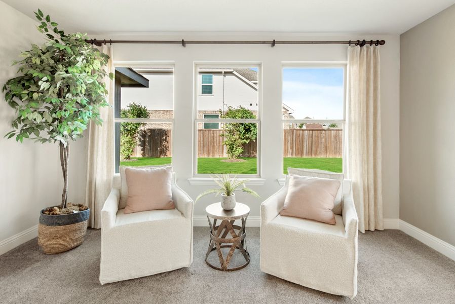 Sitting area with two white armchairs, small side table, and large windows overlooking a fenced backyard