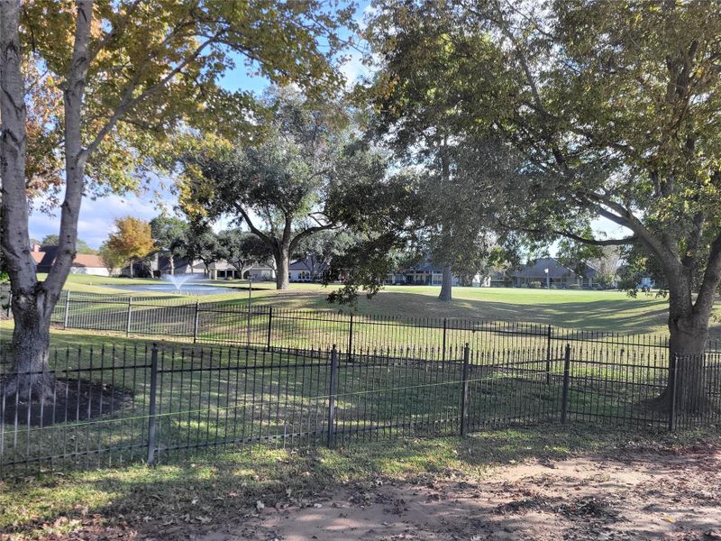 Serene, spacious backyard with a well-maintained lawn and mature trees providing ample shade. A decorative metal fence outlines the property, and a fountain adds charm to the landscape, creating a peaceful and inviting space. Golf course and water fountain views! Serene, spacious backyard with a well-maintained lawn and mature trees providing ample shade. A decorative metal fence outlines the property, and a fountain adds charm to the landscape, creating a peaceful and inviting space. Golf course and water fountain views!