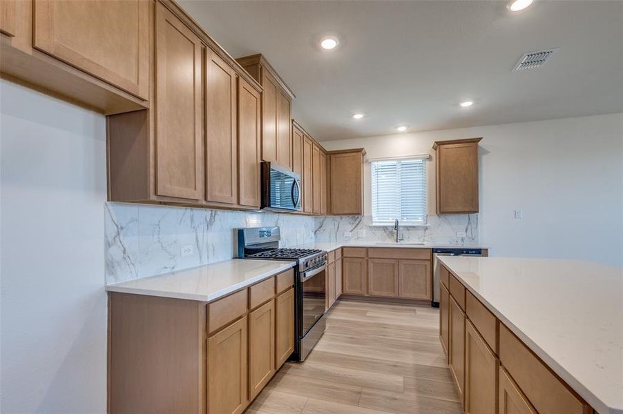 Kitchen featuring stainless steel appliances, backsplash, light wood finished floors, light countertops, and recessed lighting