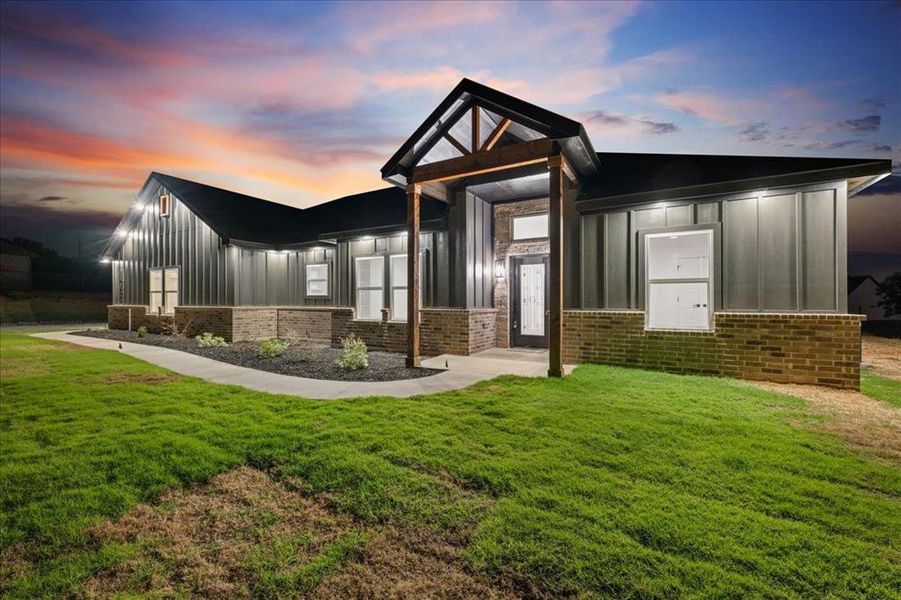 View of front facade with siding, brick accents, landscaped yard, and bright down-lights