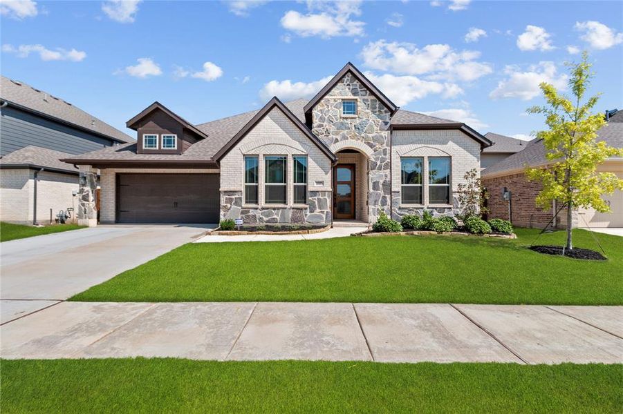 French country home with brick siding, stone siding, driveway, a front yard, and a shingled roof