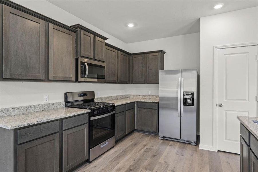 Kitchen with appliances with stainless steel finishes, light stone countertops, light wood-style flooring, and recessed lighting Kitchen with appliances with stainless steel finishes, light stone countertops, light wood-style flooring, and recessed lighting