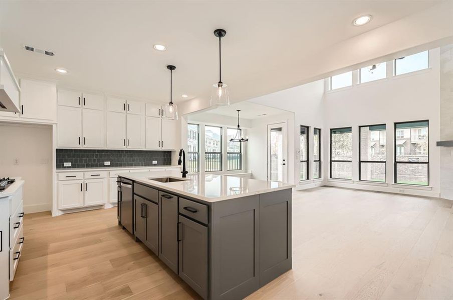 Kitchen featuring a center island with sink, decorative light fixtures, sink, light hardwood / wood-style floors, and white cabinets