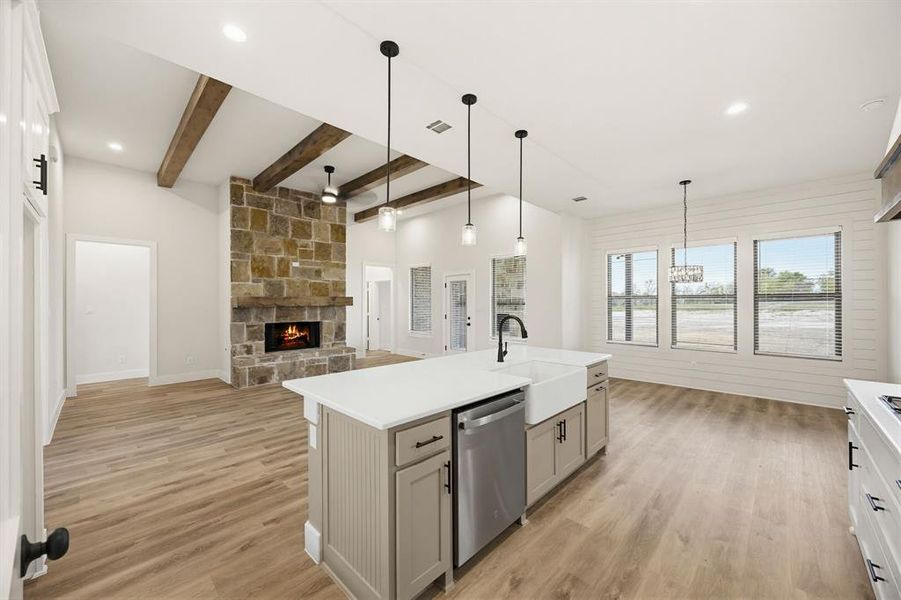 Open-concept living space featuring a stone fireplace with a substantial mantel, vaulted ceilings with exposed wood beams, and wood-finish flooring