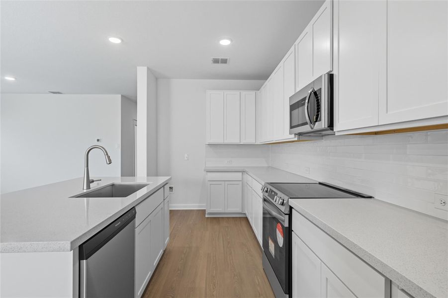 Kitchen with appliances with stainless steel finishes, light wood finished floors, white cabinets, recessed lighting, and a center island with sink Kitchen with appliances with stainless steel finishes, light wood finished floors, white cabinets, recessed lighting, and a center island with sink