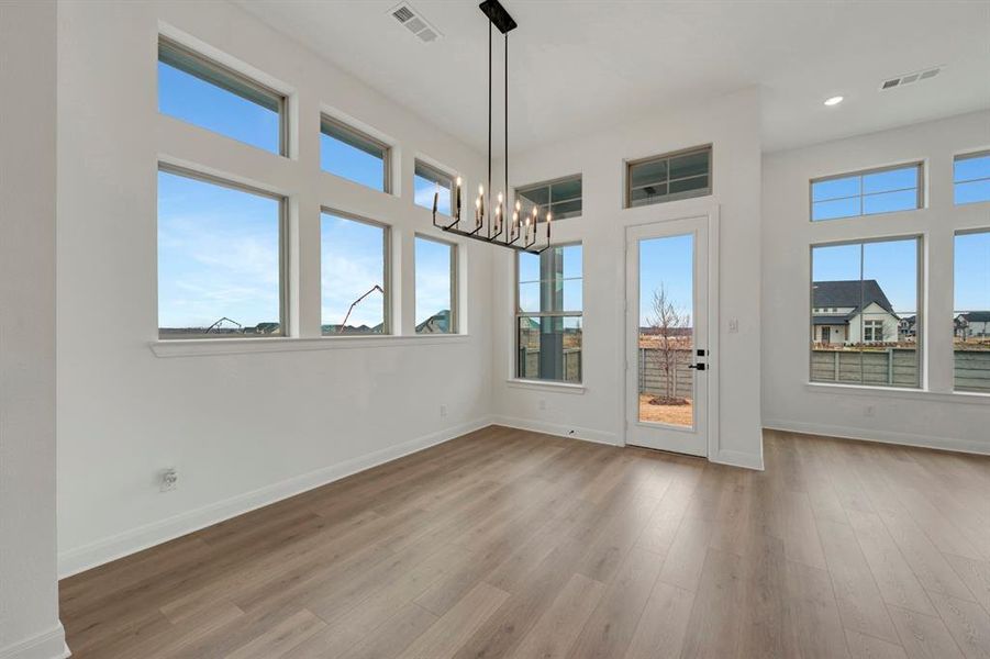 Unfurnished dining area with suspended lighting, dark wood-type flooring, plenty of natural light, and a high ceiling
