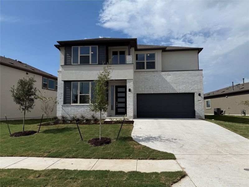 View of front facade featuring brick siding, driveway, an attached garage, a front lawn, and stucco siding View of front facade featuring brick siding, driveway, an attached garage, a front lawn, and stucco siding