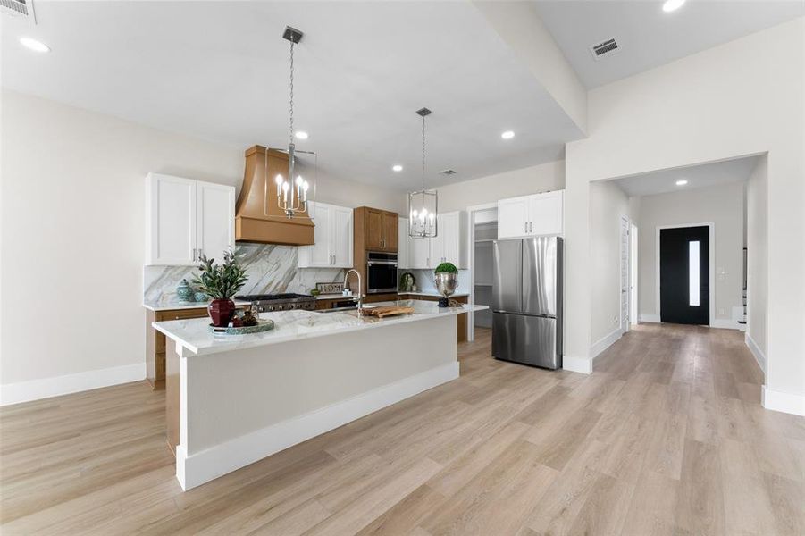 Kitchen featuring decorative light fixtures, stainless steel appliances, decorative backsplash, white cabinetry, and an island with sink Kitchen featuring decorative light fixtures, stainless steel appliances, decorative backsplash, white cabinetry, and an island with sink