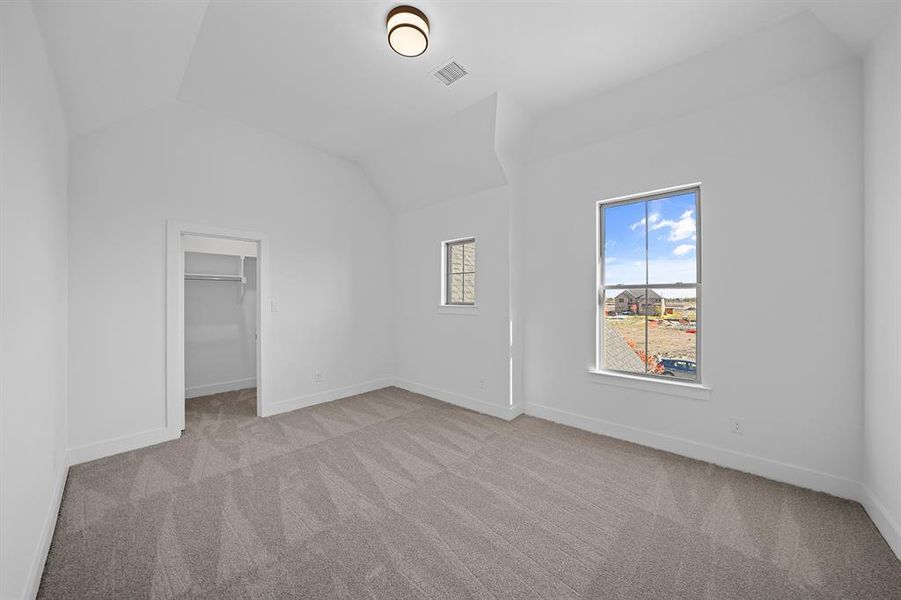 Unfurnished bedroom with light carpet, a walk in closet, and lofted ceiling