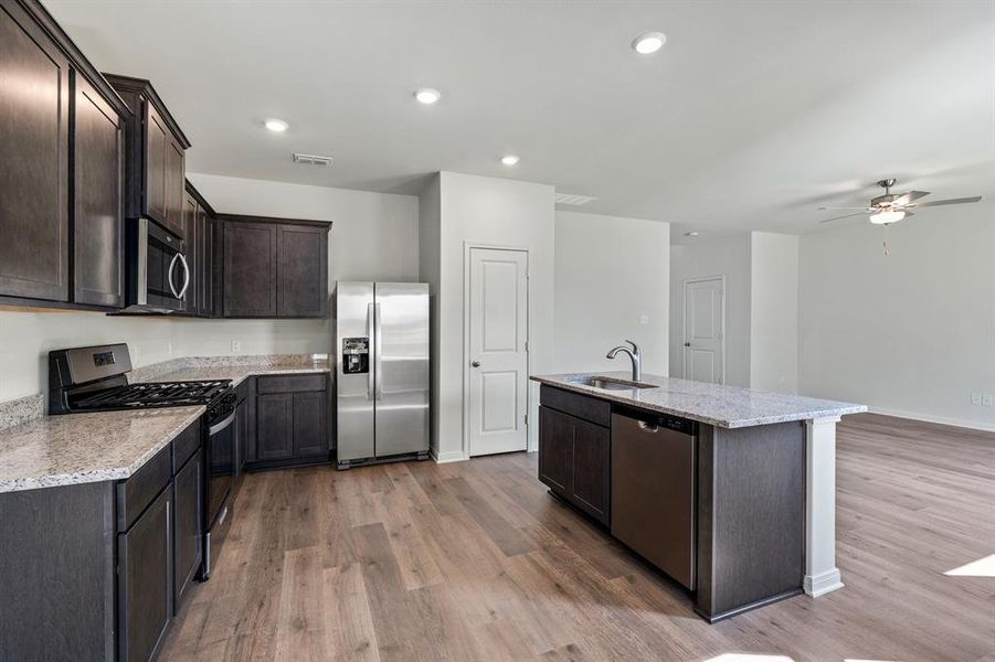 Kitchen featuring stainless steel appliances, light stone counters, dark brown cabinetry, dark wood-type flooring, and recessed lighting