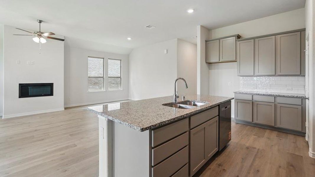 Kitchen featuring gray cabinets, light stone countertops, a glass covered fireplace, ceiling fan, and light wood finished floors
