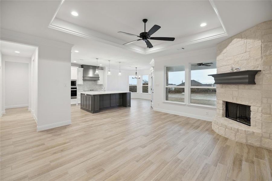 Unfurnished living room featuring a fireplace, light hardwood / wood-style flooring, ceiling fan, and a tray ceiling