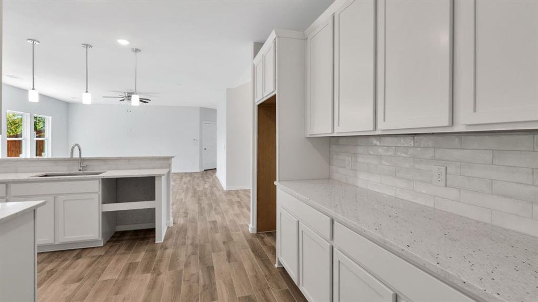 Kitchen featuring white cabinetry, light stone countertops, light wood-type flooring, ceiling fan, and sink