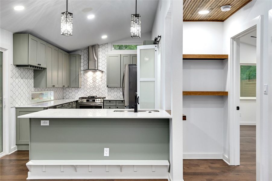 Kitchen featuring wall chimney range hood, a sink, stainless steel appliances, open shelves, and gray cabinets
