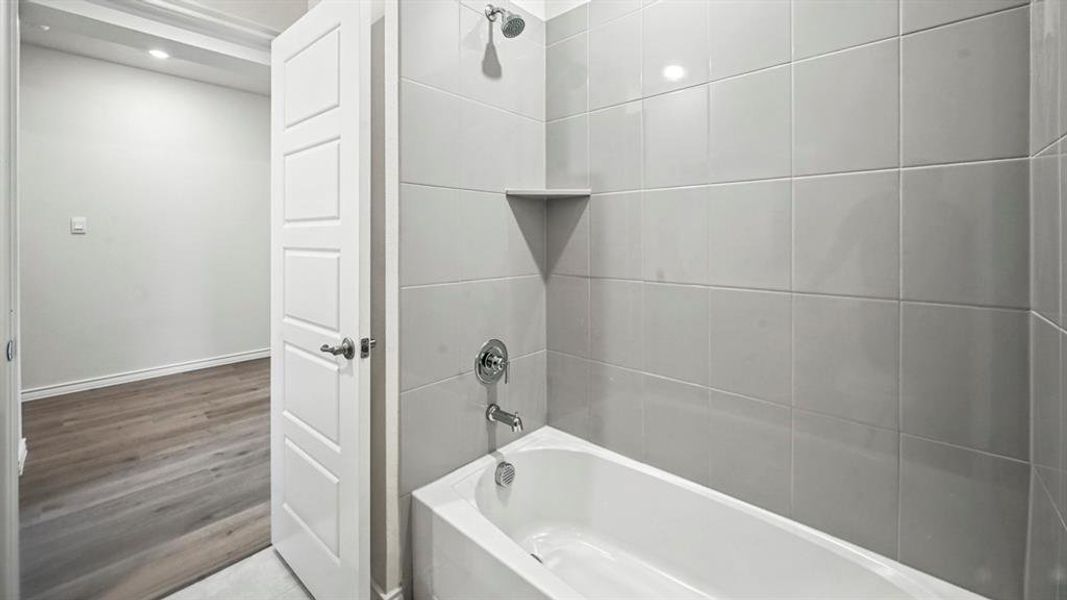 Bathroom featuring a white tub, chrome fixtures, and light gray tiled shower surround with an integrated corner shelf