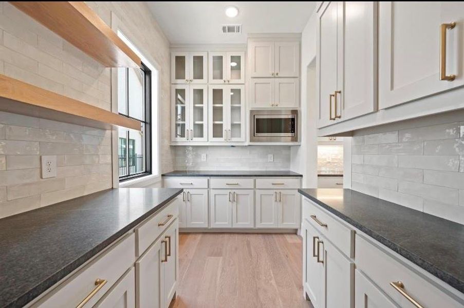 Kitchen with light wood-type flooring, decorative backsplash, stainless steel microwave, and white cabinets