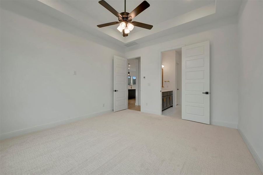 Spacious room featuring light-colored carpeting and a tray ceiling with a dark-toned ceiling fan
