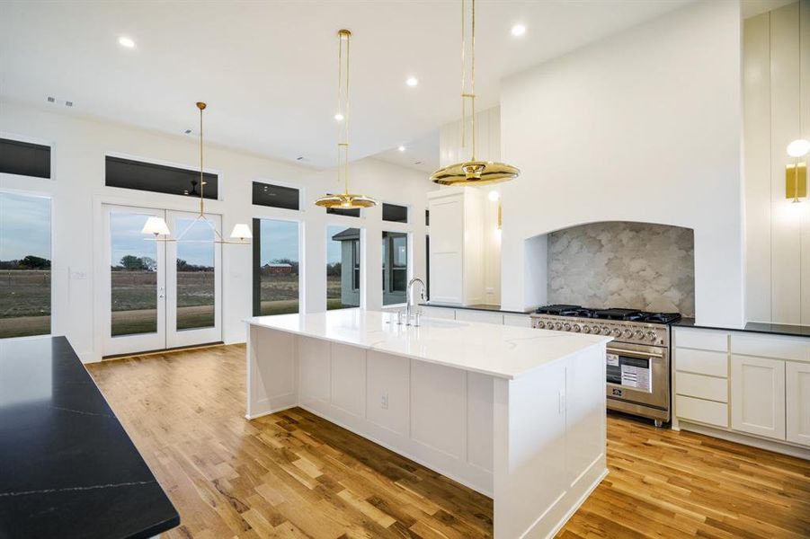 Kitchen with decorative light fixtures, a spacious island, high end stainless steel range oven, and light hardwood / wood-style flooring