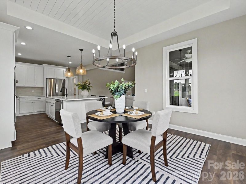 Elegant dining area offers a warm and inviting space to gather, highlighted by designer lighting, tray ceiling detail, and seamless flow into the gourmet kitchen.