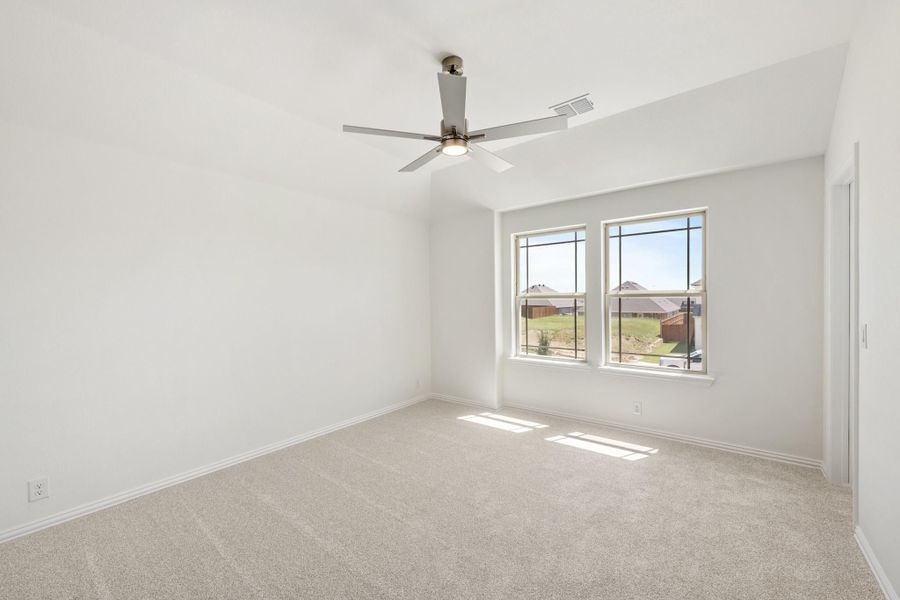 Empty bedroom with vaulted ceiling, ceiling fan, carpet flooring, and two windows with neighborhood view Empty bedroom with vaulted ceiling, ceiling fan, carpet flooring, and two windows with neighborhood view
