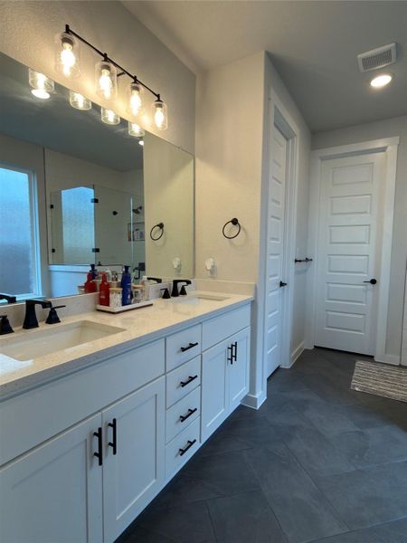 Double vanity featuring white shaker-style cabinetry, dark stone-finish countertops, and matte black fixtures