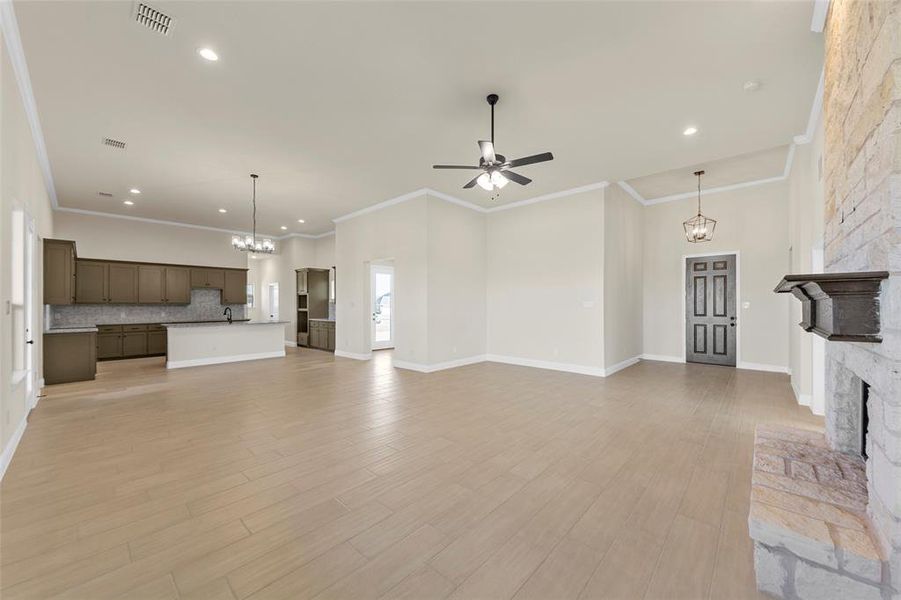 Unfurnished living room with suspended lighting, ceiling fan, light wood-type flooring, a fireplace, and ornamental molding Unfurnished living room with suspended lighting, ceiling fan, light wood-type flooring, a fireplace, and ornamental molding