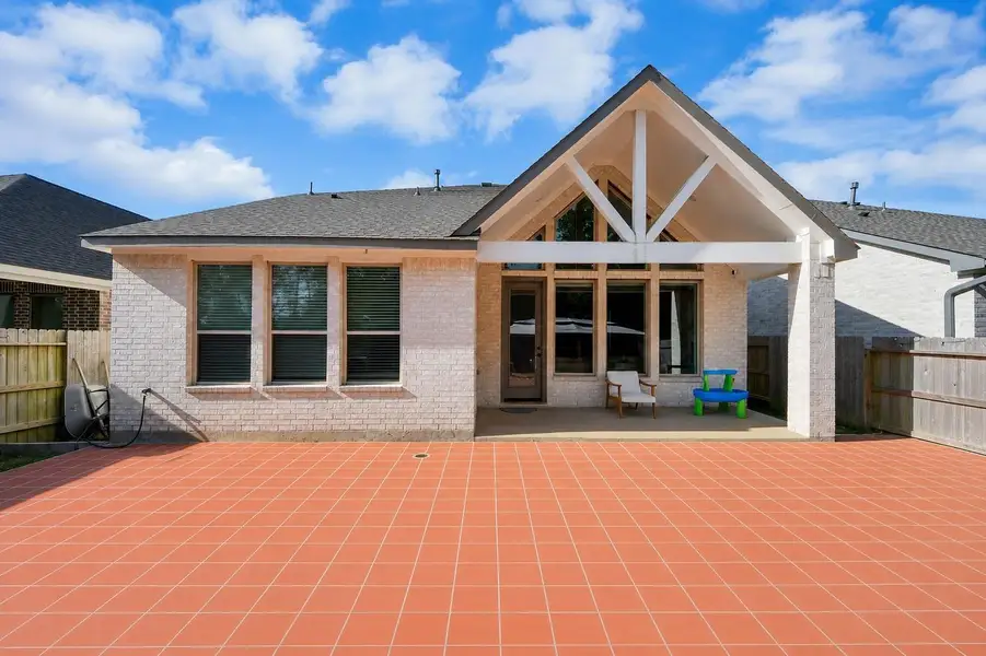This photo shows the back of a modern home with a spacious red-tiled patio, covered porch, and large windows. The yard is fenced, offering privacy and a great space for outdoor activities. This photo shows the back of a modern home with a spacious red-tiled patio, covered porch, and large windows. The yard is fenced, offering privacy and a great space for outdoor activities.