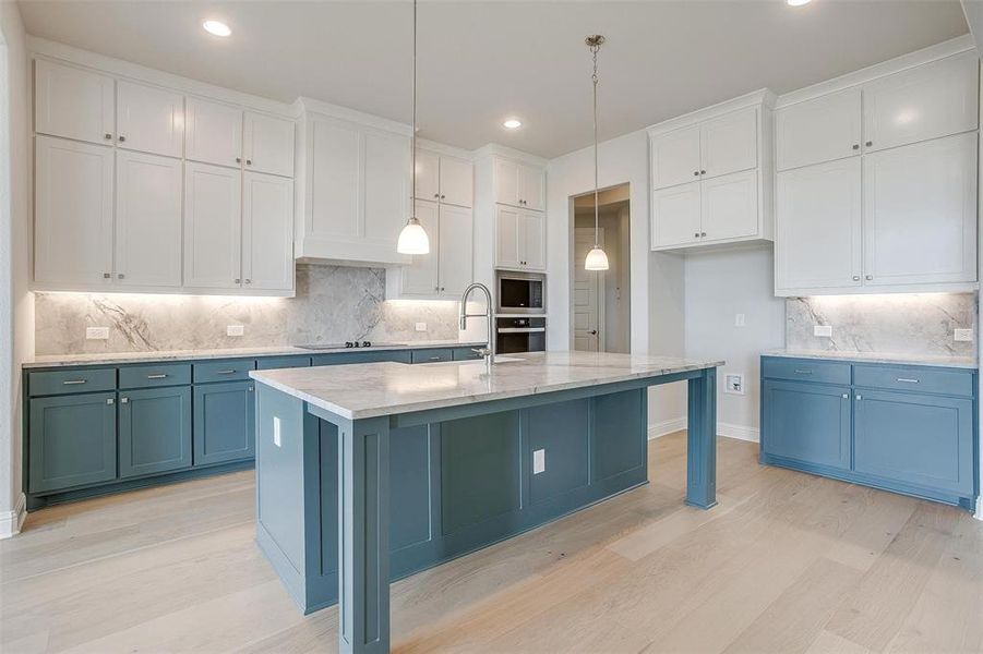 Kitchen featuring tasteful backsplash, appliances with stainless steel finishes, white cabinetry, a kitchen island with sink, and decorative light fixtures