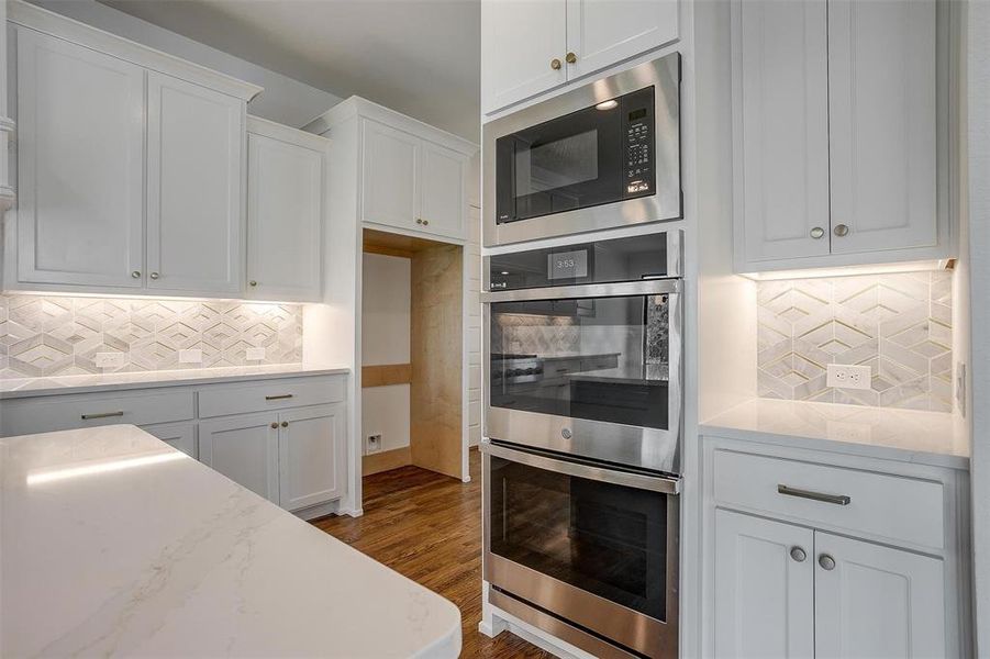 Kitchen featuring double oven, backsplash, hardwood / wood-style flooring, black microwave, and white cabinets