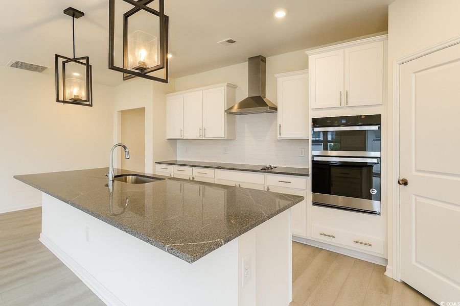 Kitchen with tasteful backsplash, wall chimney exhaust hood, light wood-type flooring, double oven, and recessed lighting Kitchen with tasteful backsplash, wall chimney exhaust hood, light wood-type flooring, double oven, and recessed lighting