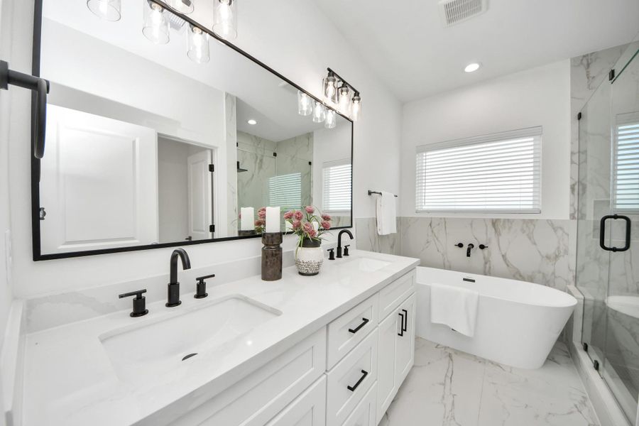 This modern bathroom features a double vanity with sleek black fixtures, a large mirror, and elegant lighting. It includes a freestanding bathtub, a spacious glass-enclosed shower, and stylish marble accents throughout.